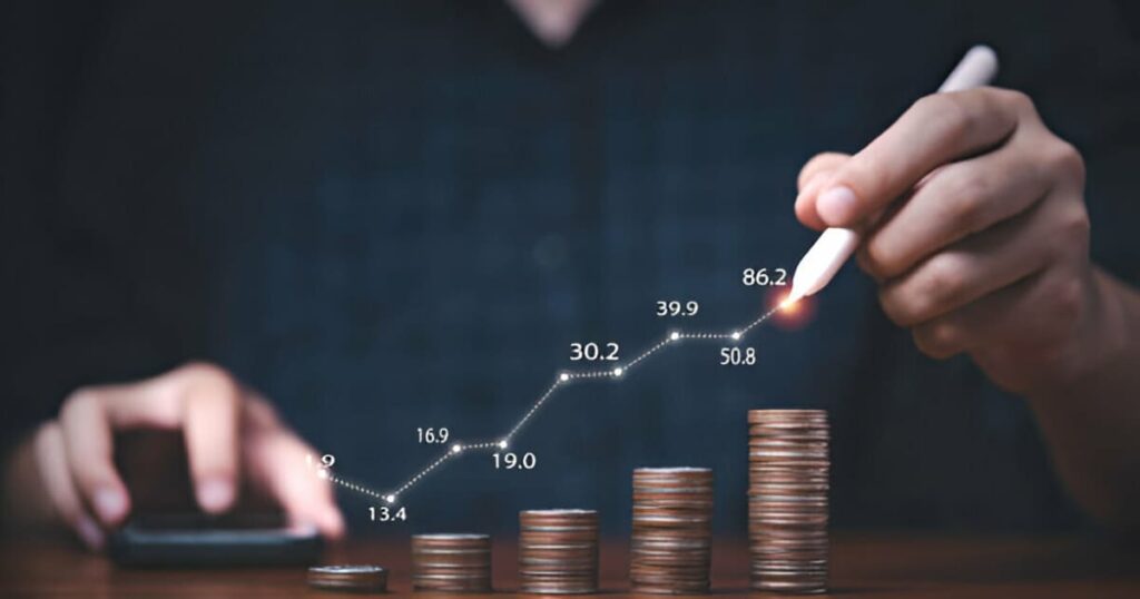 Manos de hombre con calculadora y trazando una gráfica sobre pilas ascendentes de monedas