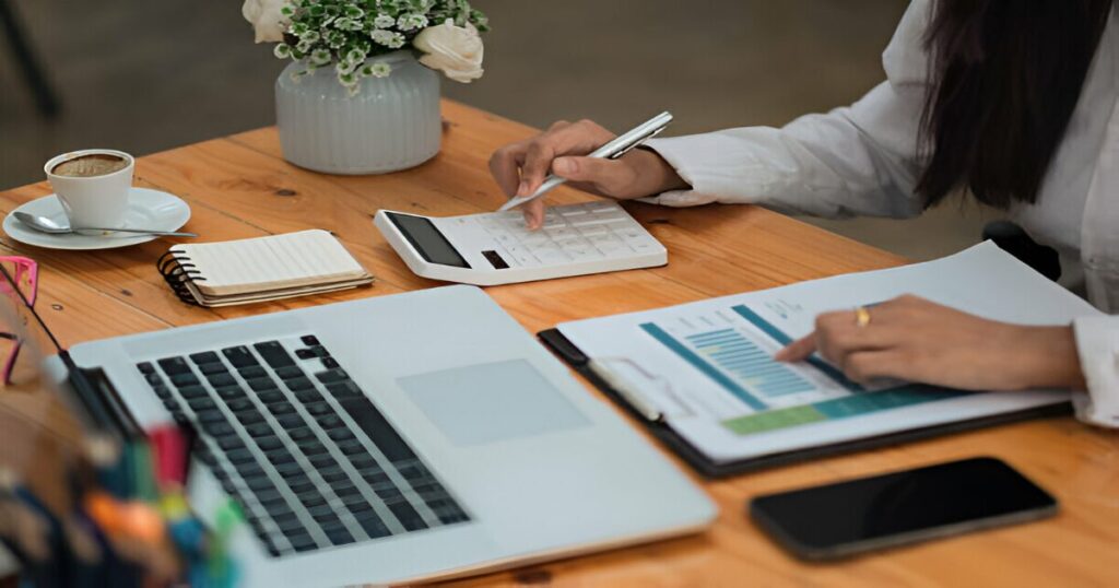Persona escribiendo en libreta conceptos financieros básicos y calculadora sobre escritorio