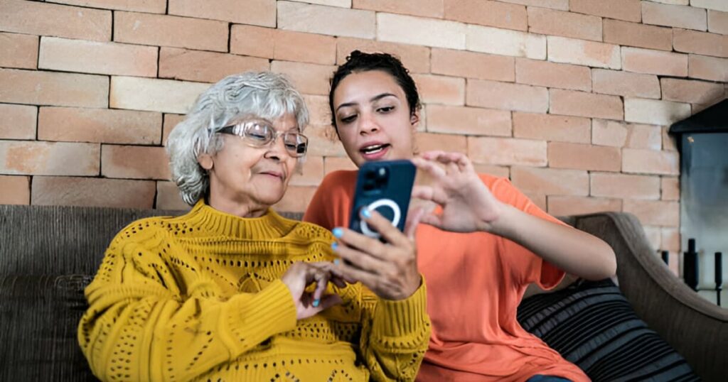 Mujer joven enseñando a una anciana a usar el celular