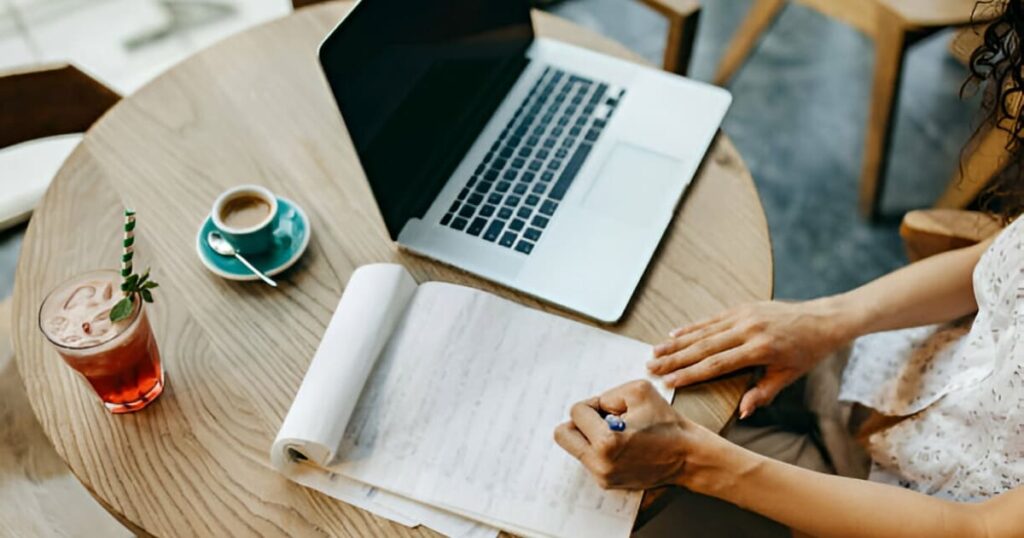 Mujer trabajando en su computadora y redactando en un cuaderno