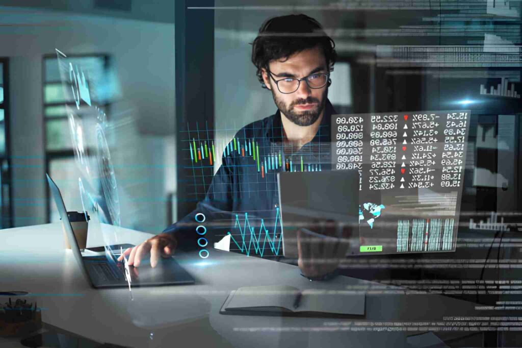 Hombre con lentes y barba analizando gráficos virtuales frente a escritorio, laptop, tableta electrónica y libreta de notas