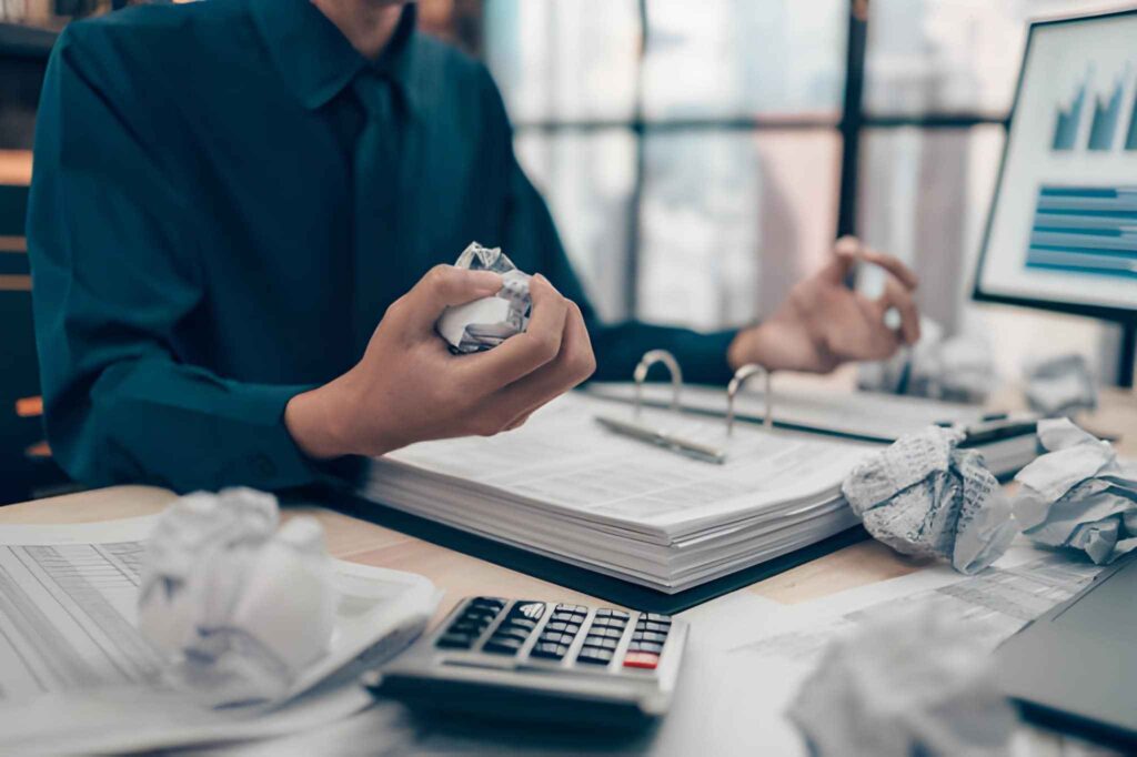 Persona con bola de papel en su mano en escritorio con documentos y otras bolas de papel
