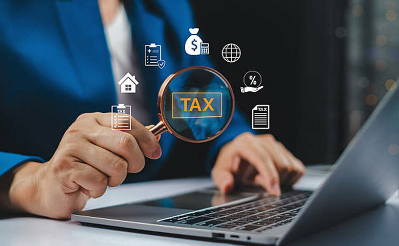 Persona frente a laptop con lupa y esquemas virtuales que aluden a impuestos - Cierre fiscal