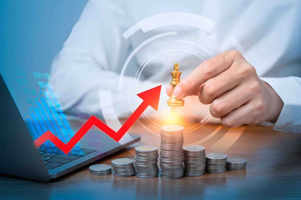 Persona sujetando pieza de ajedrez dorada sobre pilas de monedas junto a laptop y flecha roja en zig zag ascendente