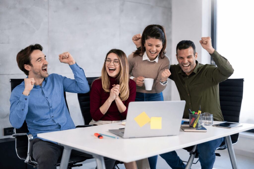 Dos mujeres y dos hombres celebrando un éxito frente a escritorio y laptop 
