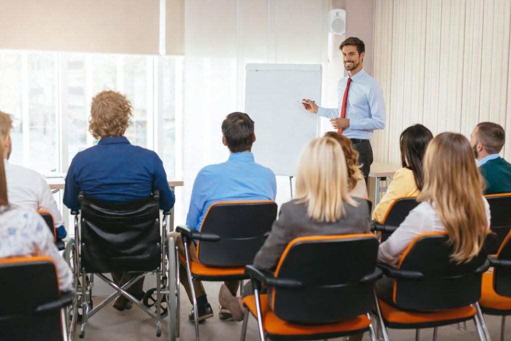 Hombre sonriente y barbado explicando a grupo sentado durante capacitación de personal