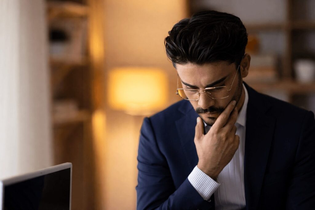 Hombre joven con barba y lentes agachado y preocupado